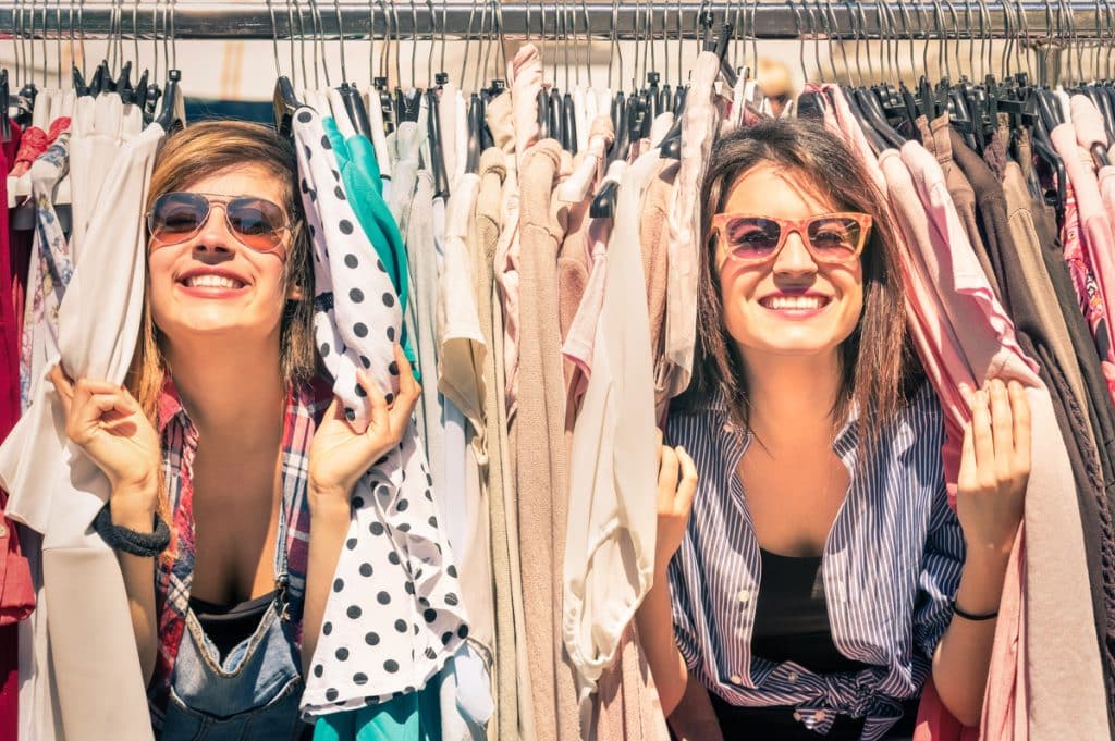 Deux femmes souriantes devant un portant à vêtements.